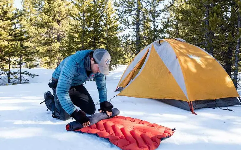 Man deflates air mattress after sleeping in tent on a winter day