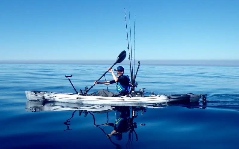 Man paddles in kayak with fishing equipment
